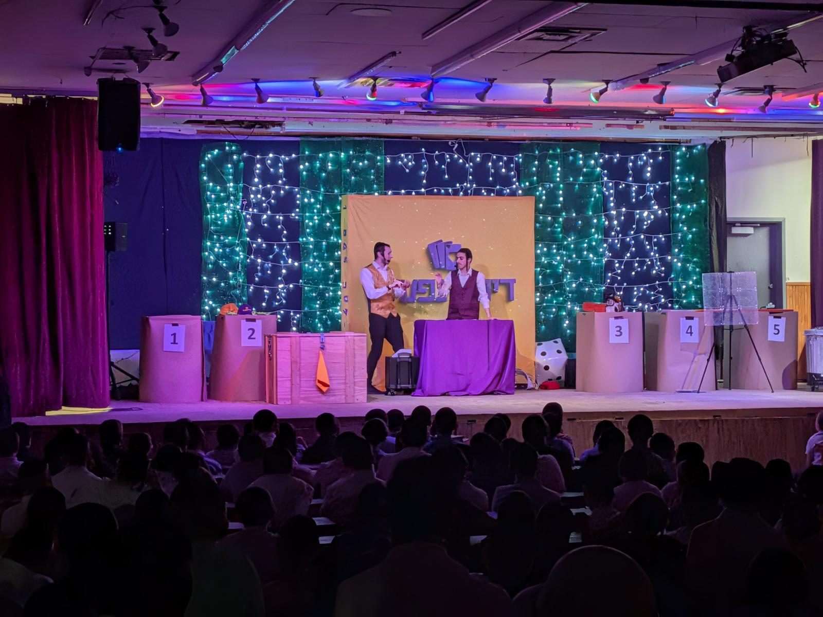 Stage show under purple lights with a row of numbered boxes in a packed hall